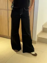 Pantalón negro de corte ancho confeccionado en mezcla de algodón y lino, con pinzas debajo de la rodilla, bordado de monograma en el bolsillo delantero y pespuntes a contratono.