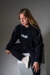 Canguro negro unisex con capucha, cordón ajustable y bolsillo tipo canguro. Estampa frontal con el logo de la marca en blanco.