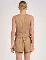 Chaleco color beige de estilo formal, con escote en V y cierre frontal de botones. Presenta bolsillos falsos a la altura de la cintura.