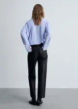 Pantalón largo de tiro alto color negro, con efecto piel, diseño recto, cinco bolsillos, trabillas y cierre de cremallera y botón.