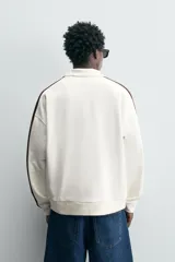 Sudadera color crudo de corte relaxed fit, con cuello alto con cremallera y mangas largas con banda marrón a contraste.