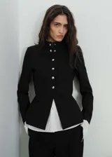 Chaqueta negra entallada con cuello mao y cierre frontal con botones plateados.