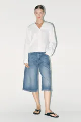 Camisa blanca de algodón con cuello bobo, manga larga con puños y cierre frontal con botones.