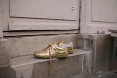 Championes deportivos de cuero y gamuza color dorado metalizado y marrón. Suela de caucho color crema con línea roja. Cordones color crema.