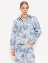 Chaqueta corta de algodón con estampado tie-dye en tonos celeste y blanco. Tiene cuello camisero, cierre con botones metálicos, bolsillos plaqué en el frente y remaches con brillos en el canesú de la espalda.