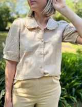Camisa color beige de mangas cortas abullonadas y cuello con puntilla bordada. Cierre frontal con botones.