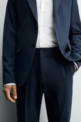 Pantalón de vestir azul marino, de corte slim fit, con bolsillos laterales y traseros. Se ajusta a la cintura con cinturón de cuero marrón.