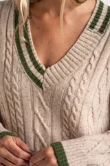 Sweater de lana y nylon color beige jaspeado, con diseño de punto trenzado (cable knit) en todo el cuerpo y mangas. Presenta cuello en V con ribete de dos franjas verdes y puños y bajo con ribete verde liso.