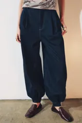 Pantalón bombacho de denim azul oscuro, tiro medio, con trabillas en la cintura, bolsillos delanteros y traseros, pespuntes marcados a contraste, bajo abullonado con puño y cierre frontal con cremallera, botón y ganchos metálicos.