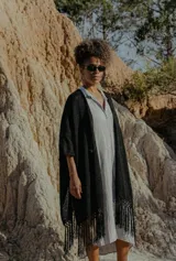 Ruana negra de tejido artesanal con flecos largos en el ruedo, de corte amplio y caída fluida.
