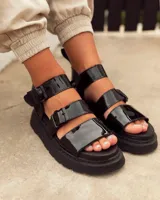 Sandalias negras charoladas con plataforma, tiras anchas y hebilla al tobillo.