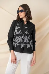 Camisa blanca de algodón con bordado floral en hilo negro en el frente. Camisa de corte clásico, con cuello abotonado, mangas largas con puños abotonados y cierre frontal con botones.