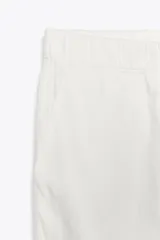 Pantalón color beige de tiro medio con cintura elástica ajustable con cordones, bolsillos delanteros y falsos bolsillos de vivo en la espalda. El bajo es ajustable con botón a presión.
