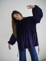Canguro oversize color violeta de plush, con capucha, bolsillo tipo canguro y cordones laterales ajustables.