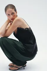 Top lencero de color marrón oscuro, con escote pico y tirantes finos. Presenta detalles de encaje a tono en el escote y en el bajo asimétrico.