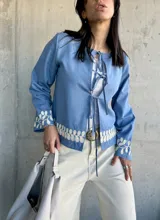 Chaqueta celeste con bordados florales blancos en el ruedo y los puños, con escote redondo y lazos para atar en el frente.