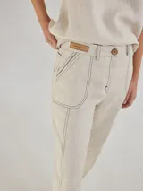 Pantalón largo color beige de lino, con bolsillos delanteros y traseros, cierre con botón y presillas para cinturón.