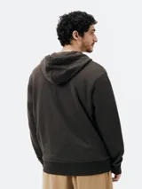 Campera marrón unisex con capucha y cierre frontal, confeccionada en algodón con felpa, corte regular fit y bolsillos tipo canguro.