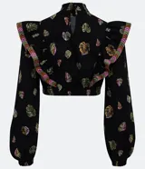 Blusa corta de tricolina negra con estampado de hojas verdes, rosadas y naranjas. Tiene cuello alto con volados y mangas largas abullonadas.