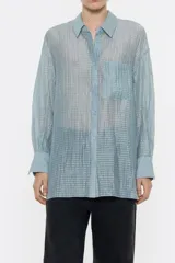 Camisa larga de viscosa con textura, de corte recto, con cuello camisero, manga larga de puño con botón y cierre frontal con abotonadura. Presenta bolsillo de plastrón en el pecho y nudo decorativo en la parte trasera para dar volumen.
