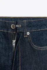 Pantalón de jean azul oscuro, de tiro medio, corte bootcut y largo hasta el tobillo. Tiene cinco bolsillos, trabillas en la cintura y cierre frontal con cremallera y botón metálico.