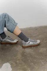 Zapatilla plateada de cuero con detalles de gamuza gris y costuras visibles.