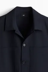 Sobrecamisa azul marino de corte recto, con cuello inglés, cierre frontal con botones, mangas largas con puños abotonados, dos bolsillos de parche en el pecho y canesú en la espalda.