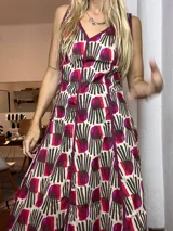 Vestido de verano con tirantes finos, escote en V ribeteado en color vino, y falda amplia con vuelo. Presenta un estampado repetitivo con formas abstractas en tonos beige, marrón oscuro y fucsia/vino.