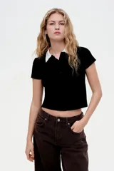 Camisa negra de punto acanalado con cuello blanco, manga corta y botonadura frontal.