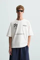 Camiseta blanca de corte holgado, cuello redondo y manga corta. Presenta estampados combinados en negro en la parte delantera y trasera.