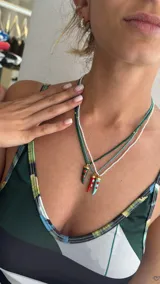 Collar tipo gargantilla compuesto por pequeñas cuentas de acrílico blancas, con dije de cuerno italiano (cornicello) esmaltado en turquesa y adornado con dos piedras rojas redondas. Los herrajes son dorados.