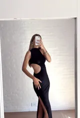 Vestido largo negro con cuello alto, sin mangas y abertura en la cintura.