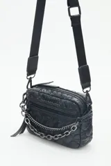 Bandolera negra de nylon matelassé con correa regulable, avíos metálicos, llavero de corazón y dijes desmontables.