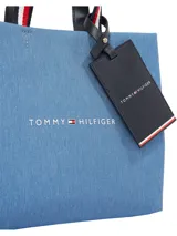 Cartera Tommy Hilfiger tipo shopper tote de tamaño mediano, confeccionada en poliéster con diseño denim azul. Tiene doble asa superior con detalle de rayas rojas, blancas y azules, correa de hombro ajustable y extraíble, cierre principal y bolsillo interno. Incluye llavero colgante con logo de la marca.