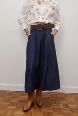 Falda larga de jean azul oscuro, corte acampanado con paneles y costuras visibles.