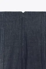 Pantalón de jean azul oscuro, de tiro muy alto y pierna ancha. Presenta pinzas en la parte delantera y cierre trasero con cremallera oculta.