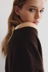 Cárdigan de punto suave color marrón oscuro, con cuello en V, botones frontales y bolsillos abiertos en la parte delantera. Presenta hombros caídos y remates acanalados en puños y bajo.