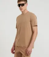Remera deportiva masculina color beige, de manga corta y cuello redondo, confeccionada con tecnología Dry. Presenta un sutil logo o estampa en el pecho.