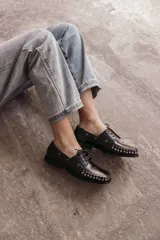 Mocasín de cuero negro con cordones y tachas metálicas en la puntera.