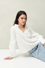 Blusa blanca de manga larga con escote en V, mangas abullonadas con volados y botones forrados.
