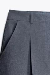 Bermudas de tiro alto color gris, con bolsillos delanteros y falso bolsillo con solapa en la espalda. Detalle de pinzas en el delantero y cierre frontal con cremallera y gancho metálico.
