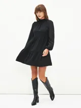 Vestido corto negro con cuello alto, mangas largas abullonadas y falda escalonada.