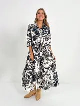 Vestido largo camisero con estampado floral en tonos rosados y blancos, con cuello camisero, manga 3/4 y falda escalonada. Incluye cinturón fino de soga.