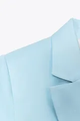 Blazer celeste de lino con cuello solapa, manga corta con hombreras, bolsillos delanteros con solapa, cintura entallada y cierre frontal con botones.