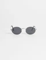 Lentes de sol con montura metálica plateada y cristales oscuros de forma ovalada.