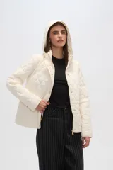 Campera blanca con diseño acolchado, cierre frontal con botones a presión y capucha desmontable.