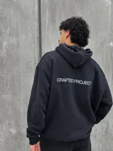 Canguro negro con capucha ajustable con cordones, bolsillo tipo canguro y estampado frontal con el texto "Crafted Project" y símbolos gráficos.