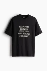 Remera negra de corte holgado con estampado frontal con la frase "Keep your friends close and your enemies far away".
