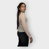 Camisa rosa pálido de tela transparente con textura y pequeños tajos en los costados. Tiene cuello clásico, mangas largas con puños abotonados y cierre frontal con botones.