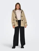 Abrigo de tela tipo teddy color beige, con capucha, cierre con botones tipo duffle coat y bolsillos frontales. Detalles en cuero sintético negro en los bordes y en los botones.